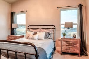 Double bed between single hung windows and lampshades on top of side tables