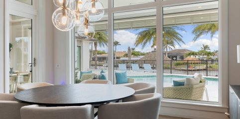 Floor-to-ceiling impact windows in a Florida dining room overlooking a pool, palm trees, and waterfront patio