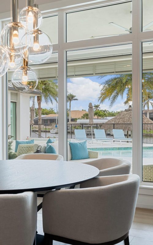 Floor-to-ceiling impact windows in a Florida dining room overlooking a pool, palm trees, and waterfront patio